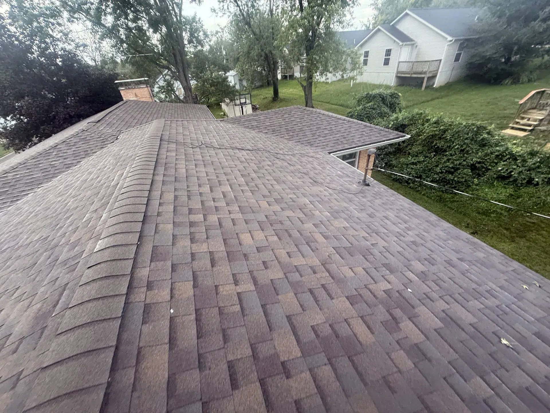 Newly installed brown architectural shingle roof with ridge caps on a brick home
