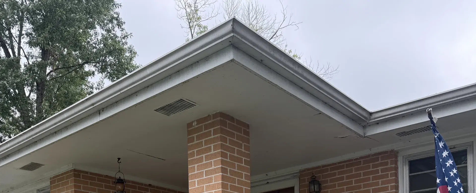 Aging white soffit and fascia with visible cracks over a brick front porch